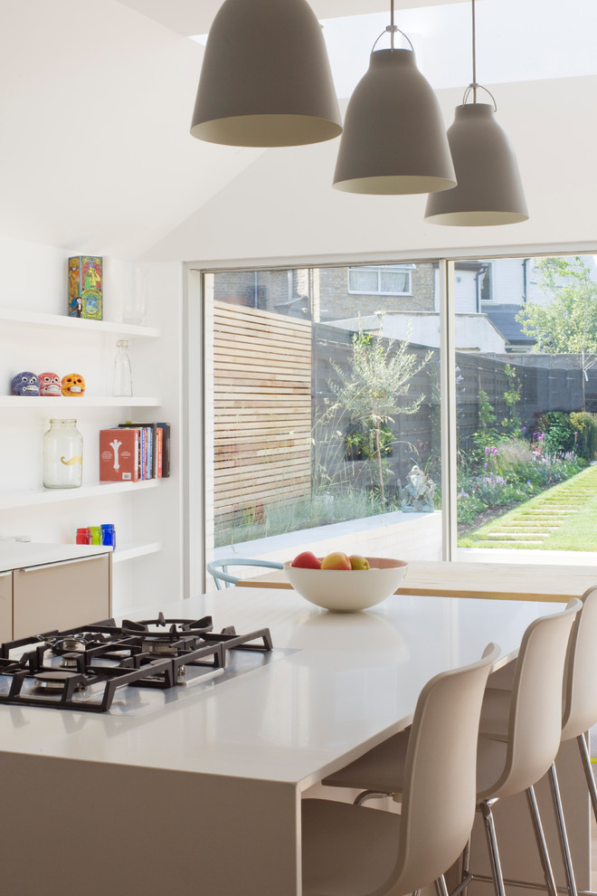 This is an example of a medium sized contemporary l-shaped kitchen/diner in London with flat-panel cabinets, grey cabinets, engineered stone countertops, an island, an integrated sink, white splashback, stainless steel appliances and light hardwood flooring.