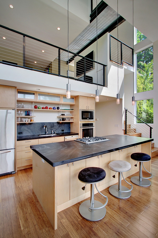 Modern galley kitchen in Seattle with open cabinets, light wood cabinets, black splashback, stone slab splashback and stainless steel appliances.