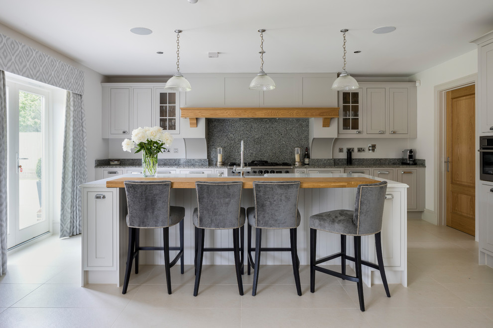 This is an example of a classic single-wall kitchen/diner in Surrey with grey cabinets, grey splashback, stainless steel appliances, a breakfast bar and beige floors.