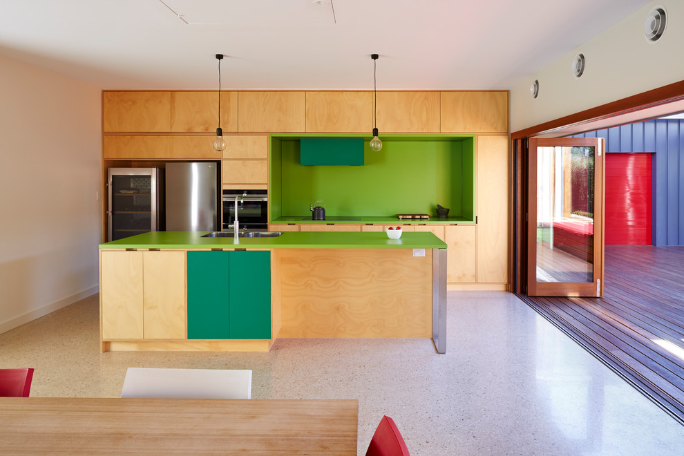 На фото: параллельная кухня-гостиная в современном стиле с двойной мойкой, плоскими фасадами, бежевыми фасадами, зеленым фартуком, техникой из нержавеющей стали, островом, бежевым полом и зеленой столешницей
