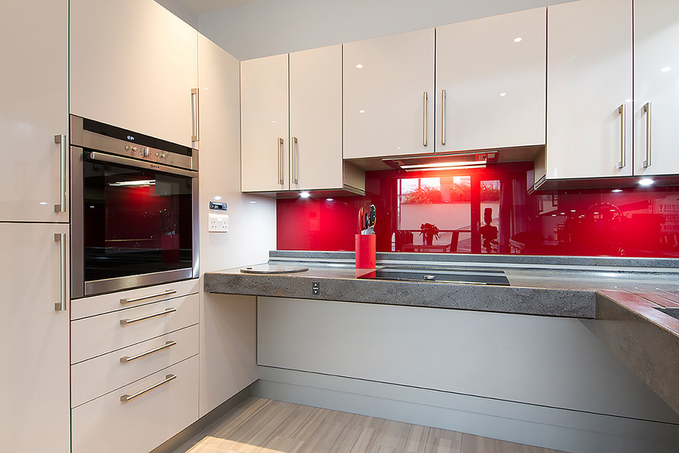 Inspiration for a small contemporary u-shaped open plan kitchen in Buckinghamshire with an integrated sink, flat-panel cabinets, white cabinets, composite countertops, red splashback, glass sheet splashback, stainless steel appliances, laminate floors, no island and beige floors.