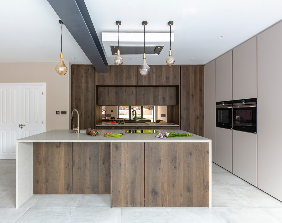 Inspiration for a large contemporary open plan kitchen in London with flat-panel cabinets, concrete worktops, mirror splashback, black appliances, an island, a submerged sink, dark wood cabinets, grey floors and grey worktops.