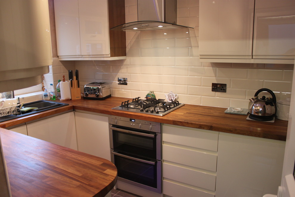 Photo of a medium sized modern u-shaped enclosed kitchen in Other with a double-bowl sink, flat-panel cabinets, white cabinets, wood worktops, white splashback, ceramic splashback, stainless steel appliances and no island.