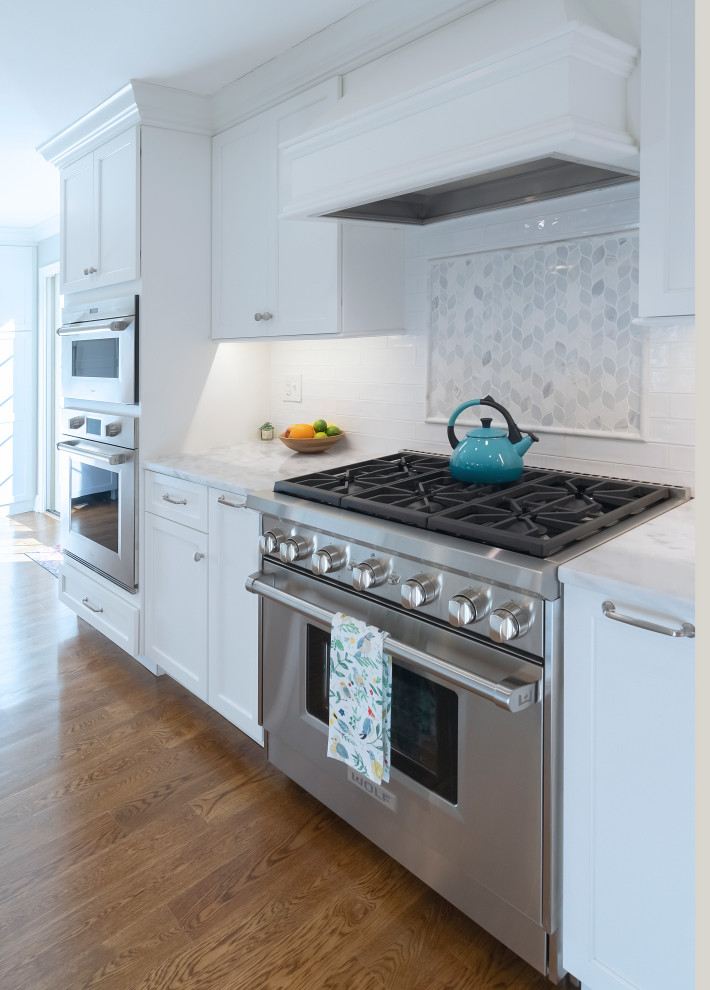 Example of a huge classic galley medium tone wood floor and brown floor open concept kitchen design in Philadelphia with an undermount sink, shaker cabinets, white cabinets, quartzite countertops, white backsplash, cement tile backsplash, stainless steel appliances, an island and white countertops