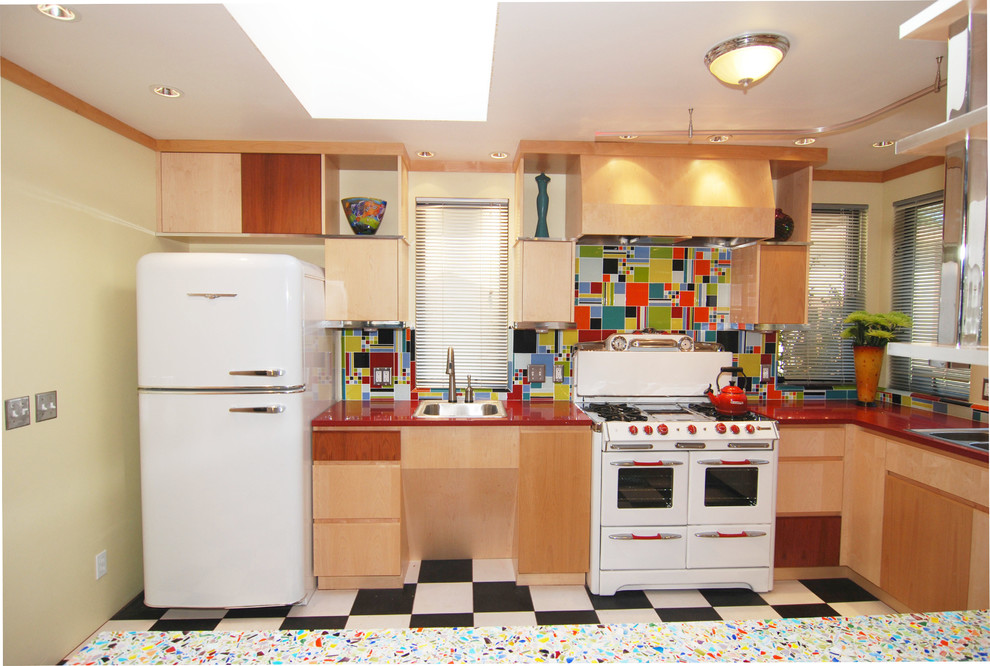 Bild på ett mellanstort funkis kök, med en dubbel diskho, släta luckor, skåp i ljust trä, bänkskiva i återvunnet glas, blått stänkskydd, stänkskydd i cementkakel, vita vitvaror, linoleumgolv och en halv köksö