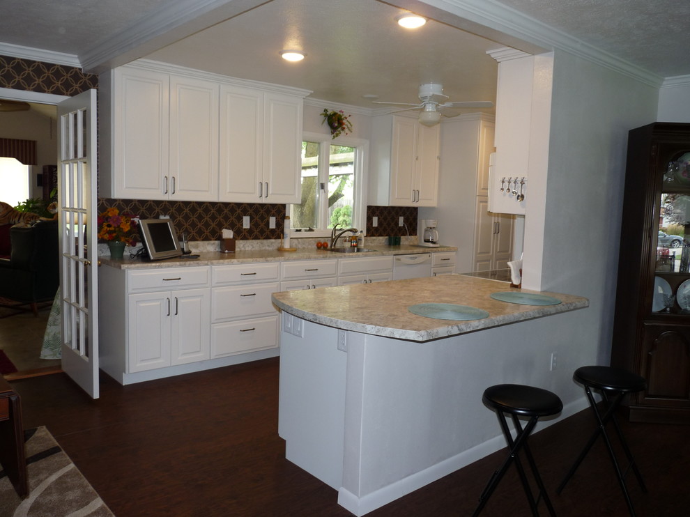 Foto på ett mellanstort vintage kök, med en undermonterad diskho, luckor med upphöjd panel, vita skåp, laminatbänkskiva, vita vitvaror, vinylgolv, en halv köksö och brunt golv