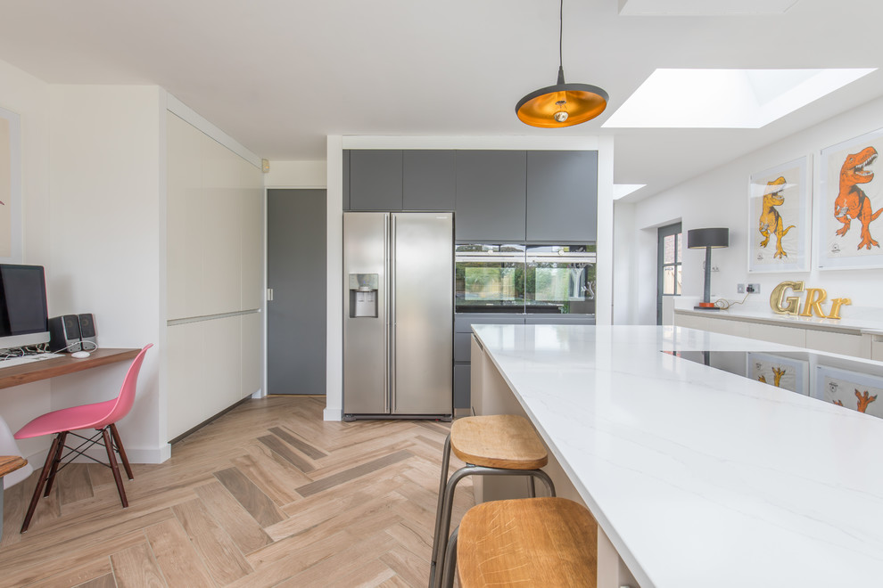 Photo of a medium sized contemporary kitchen/diner in Sussex with a built-in sink, flat-panel cabinets, grey cabinets, engineered stone countertops, white splashback, ceramic splashback, stainless steel appliances, ceramic flooring, an island and brown floors.