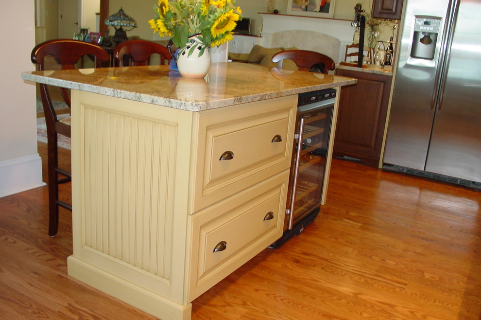 Example of a classic l-shaped eat-in kitchen design in New York with an undermount sink, raised-panel cabinets, yellow cabinets, granite countertops, white backsplash and stainless steel appliances