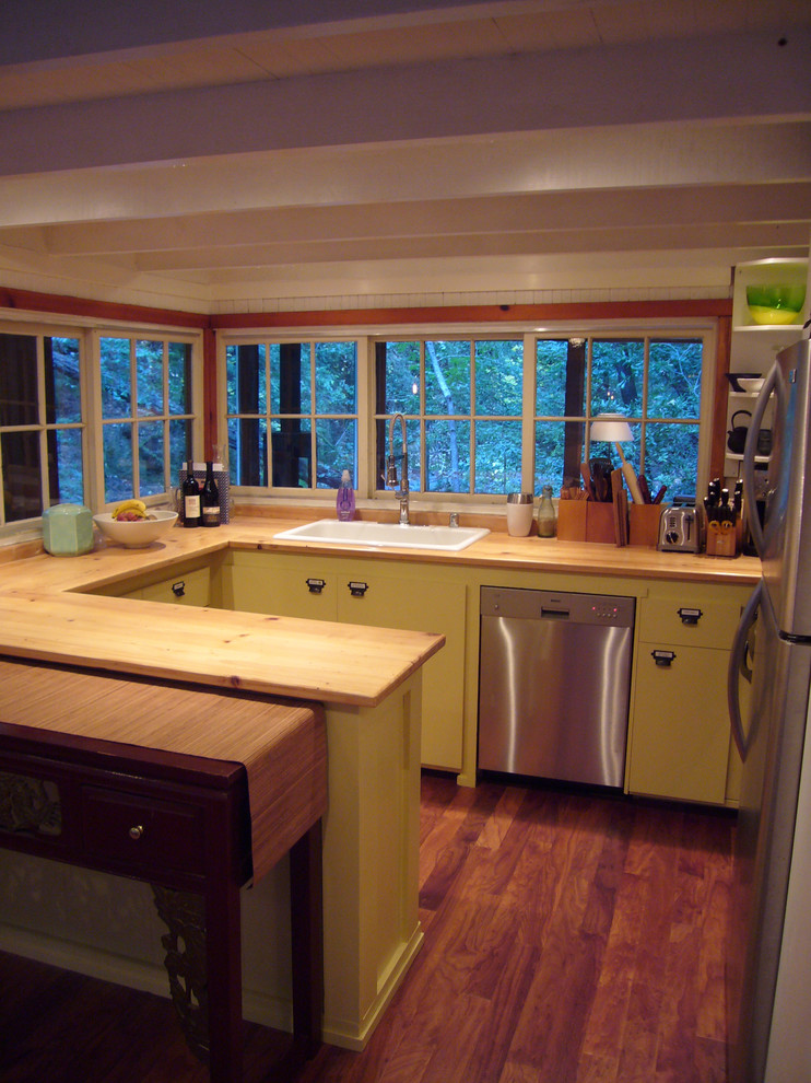 На фото: кухня в стиле рустика с желтыми фасадами, деревянной столешницей и накладной мойкой с
