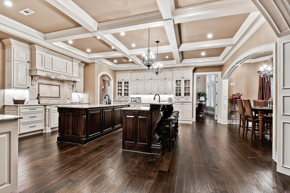 Inspiration for a huge timeless u-shaped dark wood floor and brown floor kitchen remodel in Other with an undermount sink, raised-panel cabinets, white cabinets, granite countertops, beige backsplash, stone tile backsplash, stainless steel appliances, two islands and multicolored countertops