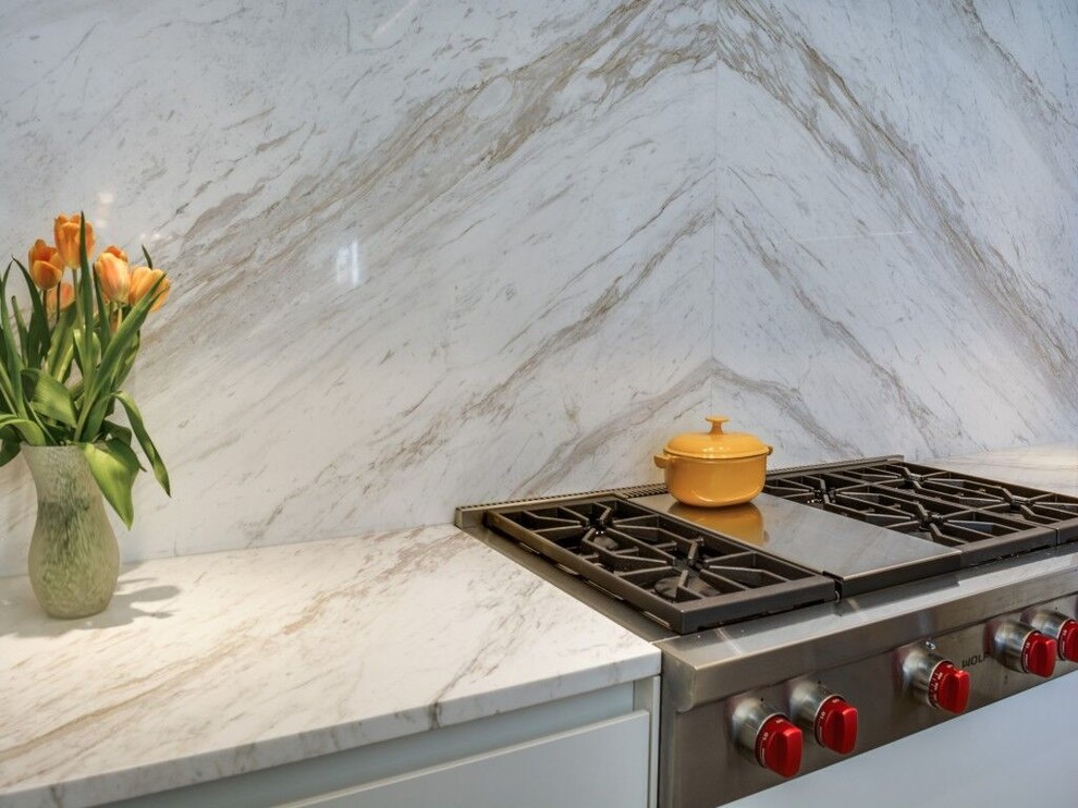 Exempel på ett avskilt, litet modernt l-kök, med en undermonterad diskho, släta luckor, vita skåp, marmorbänkskiva, vitt stänkskydd, glaspanel som stänkskydd, rostfria vitvaror, kalkstensgolv och en köksö