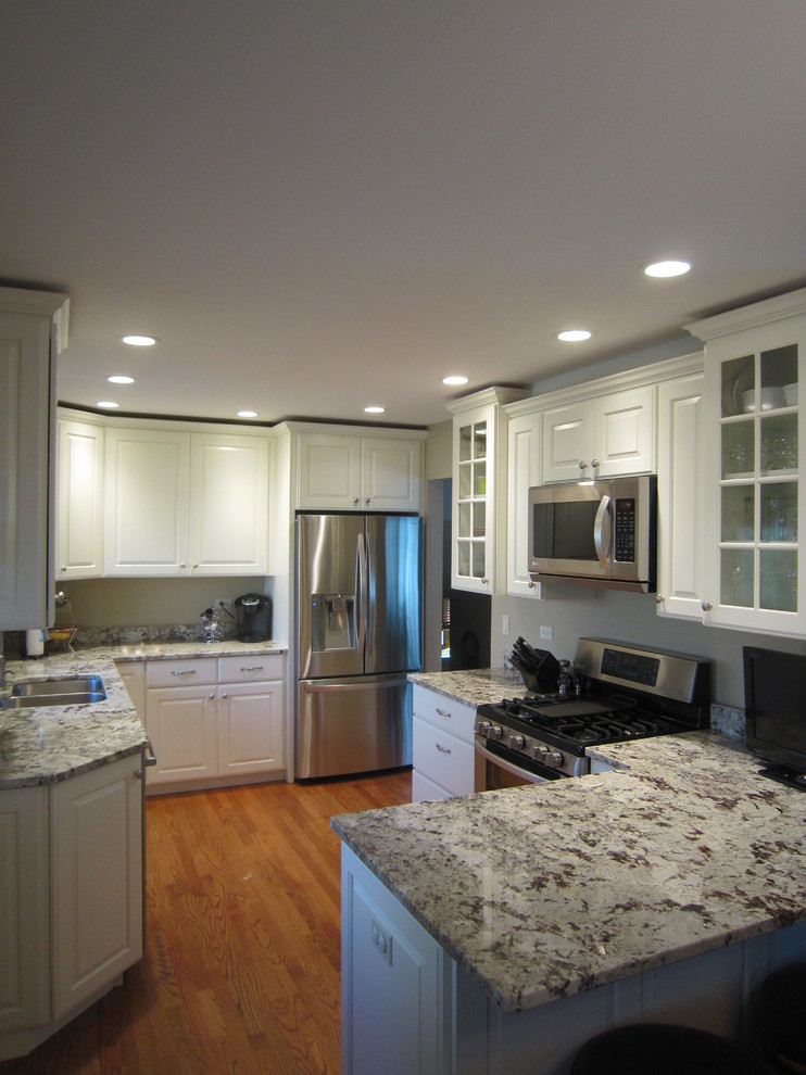 This is an example of a medium sized traditional kitchen/diner in Chicago with raised-panel cabinets, white cabinets, stainless steel appliances, medium hardwood flooring, a breakfast bar, granite worktops and a double-bowl sink.