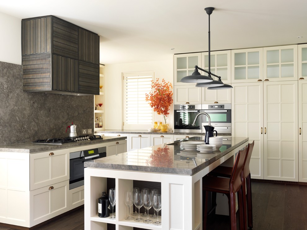 Klassisk inredning av ett mellanstort kök, med en undermonterad diskho, luckor med infälld panel, marmorbänkskiva, stänkskydd i stenkakel, mörkt trägolv, en köksö, vita skåp, grått stänkskydd och rostfria vitvaror
