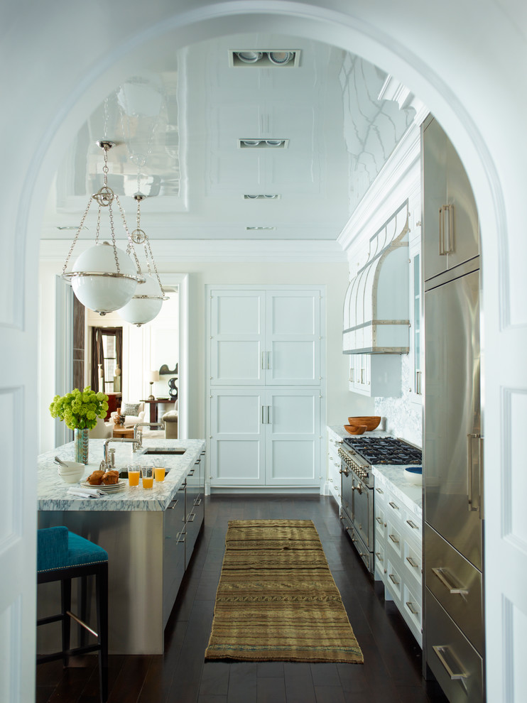 Example of a large classic galley kitchen design in New York with recessed-panel cabinets, white cabinets, white backsplash, stainless steel appliances, an island and an undermount sink