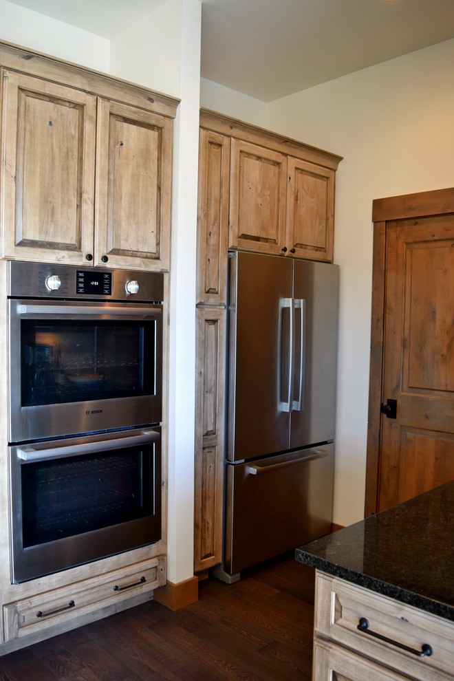 Rustic l-shaped open plan kitchen in Denver with a submerged sink, raised-panel cabinets, distressed cabinets, white splashback, stainless steel appliances, dark hardwood flooring and an island.