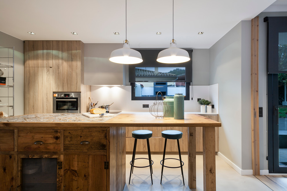 Cette image montre une grande cuisine parallèle design en bois clair fermée avec un placard à porte plane, plan de travail carrelé, une crédence blanche, un électroménager en acier inoxydable et îlot.