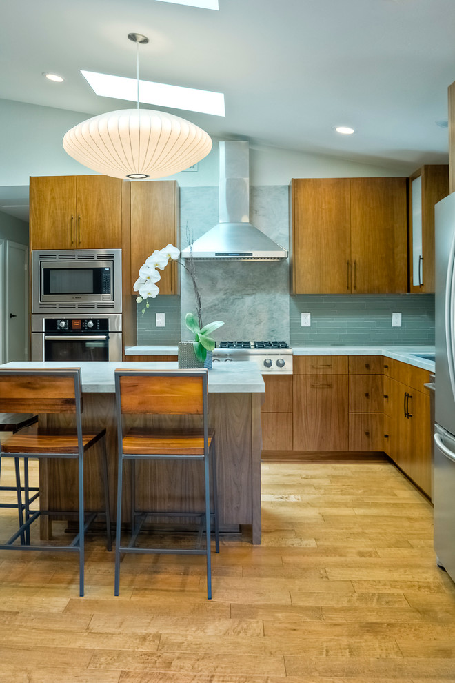 Photo of a medium sized world-inspired l-shaped kitchen/diner in San Diego with a submerged sink, flat-panel cabinets, light wood cabinets, marble worktops, green splashback, matchstick tiled splashback, stainless steel appliances, light hardwood flooring and an island.