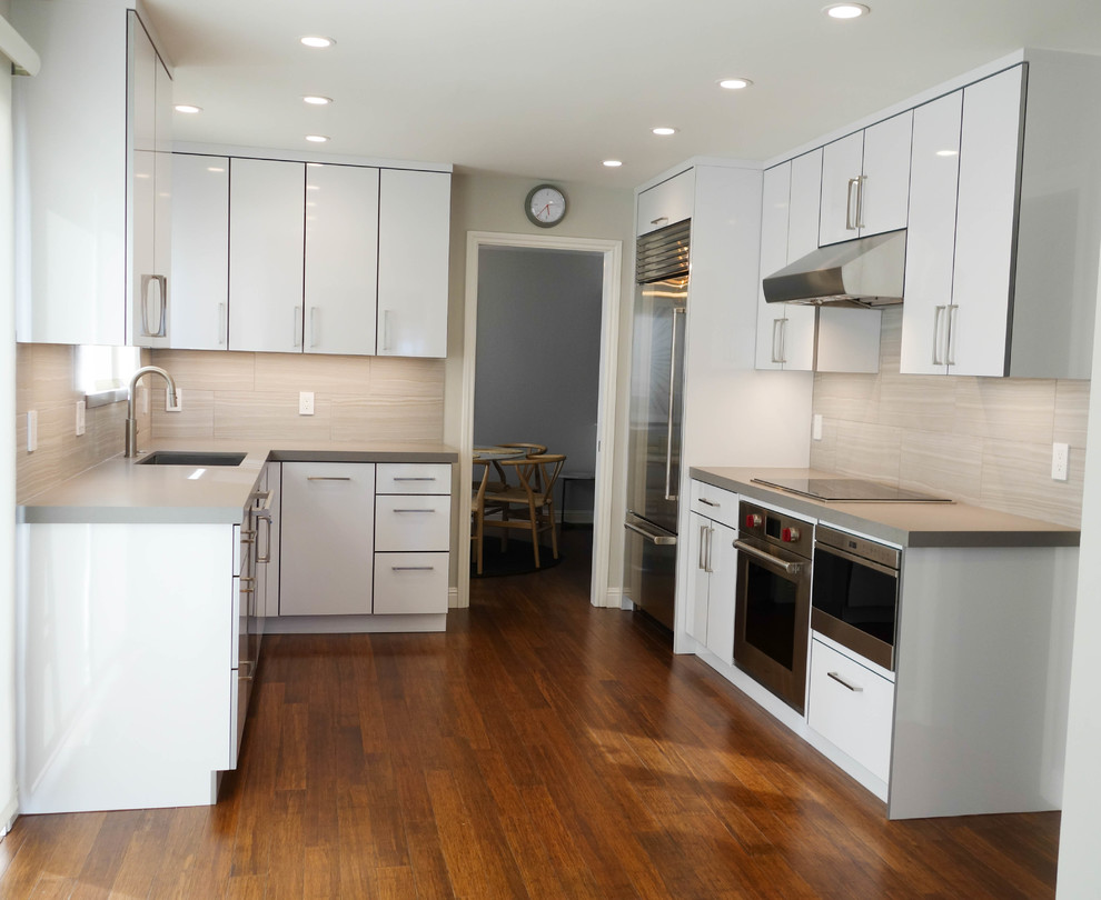 Inredning av ett modernt mellanstort grå grått kök, med en undermonterad diskho, släta luckor, vita skåp, bänkskiva i kvarts, grått stänkskydd, stänkskydd i porslinskakel, rostfria vitvaror, bambugolv och brunt golv