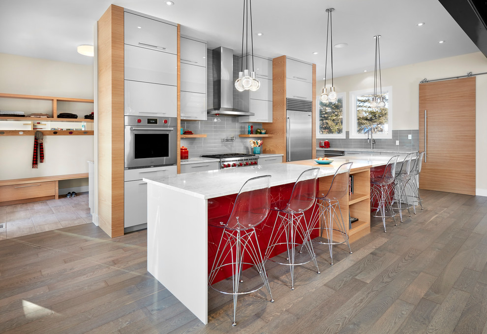 Inspiration for a contemporary kitchen in Edmonton with flat-panel cabinets, white cabinets, grey splashback, stainless steel appliances, medium hardwood flooring and an island.
