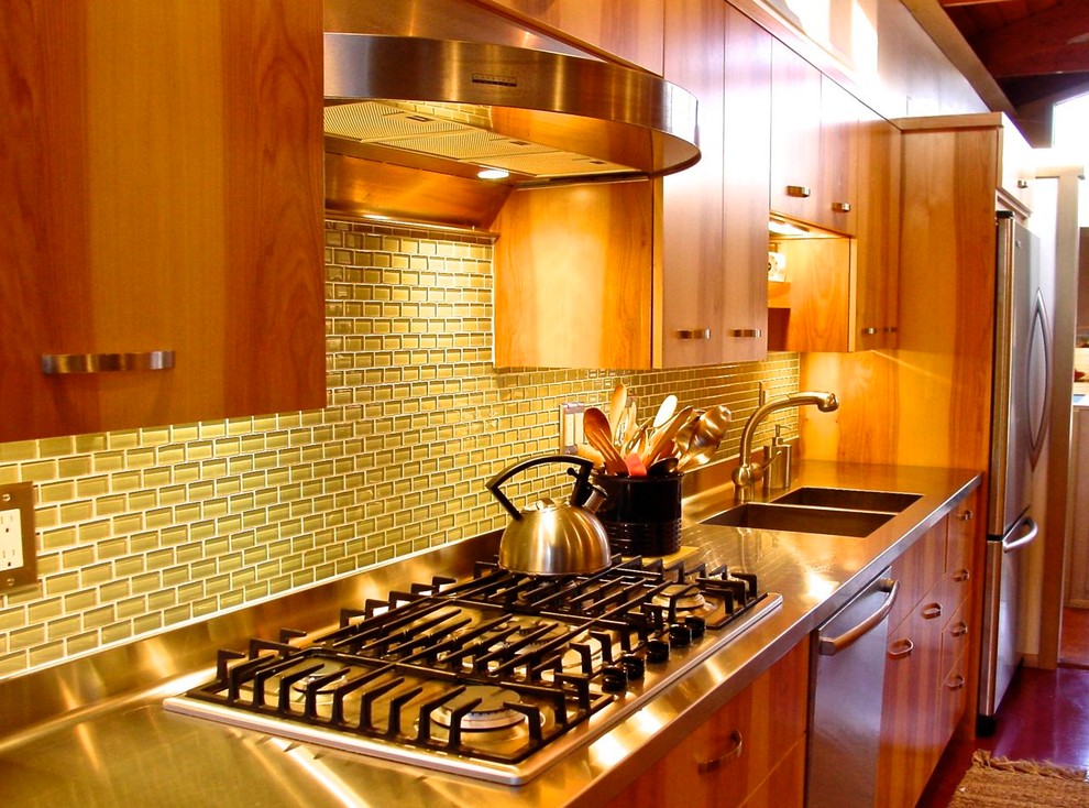 Inredning av ett modernt mellanstort linjärt kök och matrum, med en dubbel diskho, släta luckor, skåp i ljust trä, grönt stänkskydd, stänkskydd i glaskakel, rostfria vitvaror, bänkskiva i rostfritt stål, mörkt trägolv och brunt golv