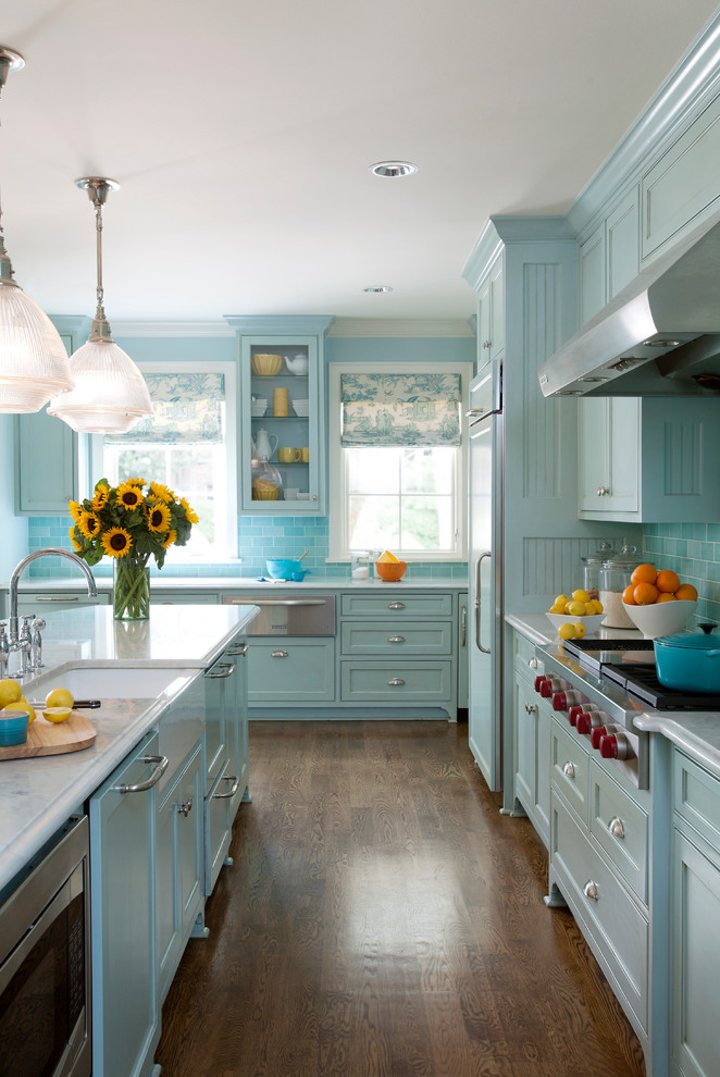 Inspiration for a transitional l-shaped medium tone wood floor open concept kitchen remodel in Little Rock with recessed-panel cabinets, blue cabinets, marble countertops, blue backsplash, ceramic backsplash, stainless steel appliances and an island