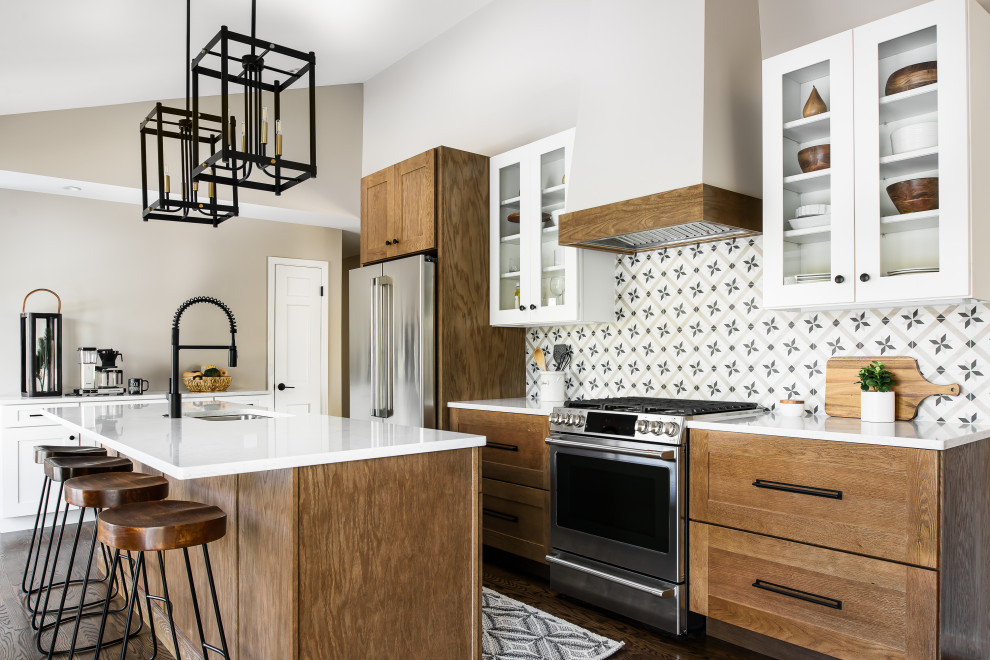 Medium sized farmhouse l-shaped kitchen/diner in St Louis with a single-bowl sink, shaker cabinets, medium wood cabinets, engineered stone countertops, porcelain splashback, stainless steel appliances, dark hardwood flooring, an island, brown floors and white worktops.
