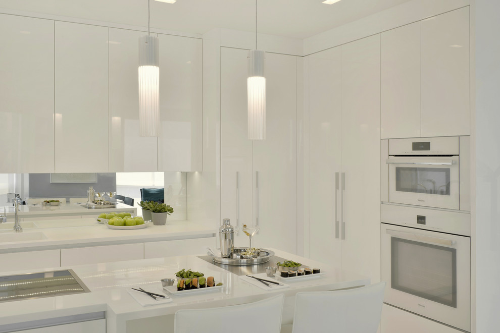 This is an example of a small contemporary l-shaped enclosed kitchen in New York with an integrated sink, flat-panel cabinets, white cabinets, composite countertops, mirror splashback, white appliances, porcelain flooring, an island and beige floors.