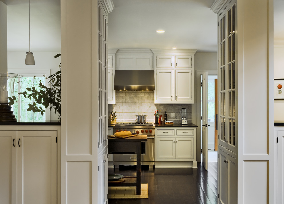 Klassisk inredning av ett kök och matrum, med luckor med infälld panel, vita skåp, vitt stänkskydd, stänkskydd i tunnelbanekakel och rostfria vitvaror
