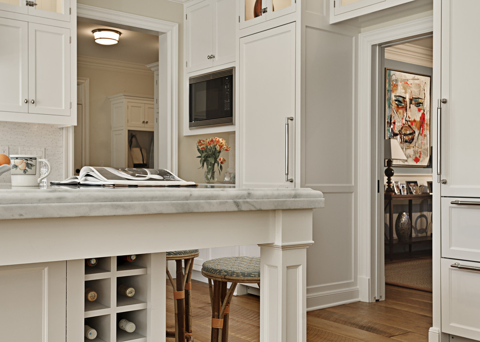 Example of a classic eat-in kitchen design in New York with a farmhouse sink, shaker cabinets, white cabinets, marble countertops, white backsplash and paneled appliances