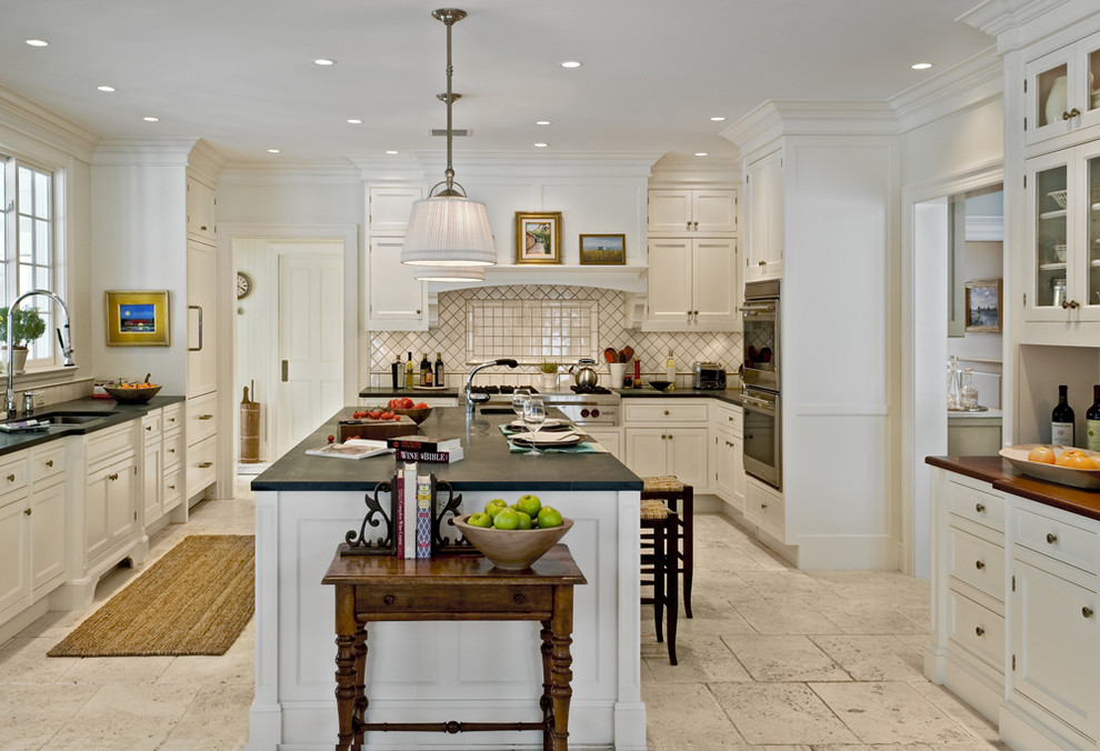 Example of a farmhouse enclosed kitchen design in New York with soapstone countertops, recessed-panel cabinets, white cabinets, white backsplash, porcelain backsplash and stainless steel appliances