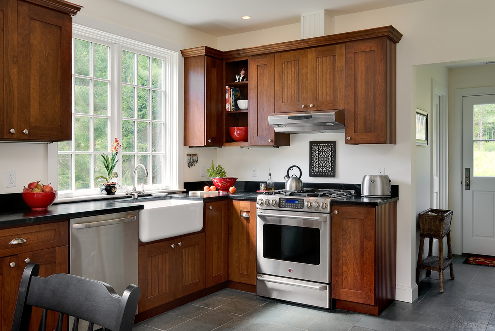 This is an example of a classic kitchen/diner in New York with a belfast sink, shaker cabinets, dark wood cabinets and stainless steel appliances.