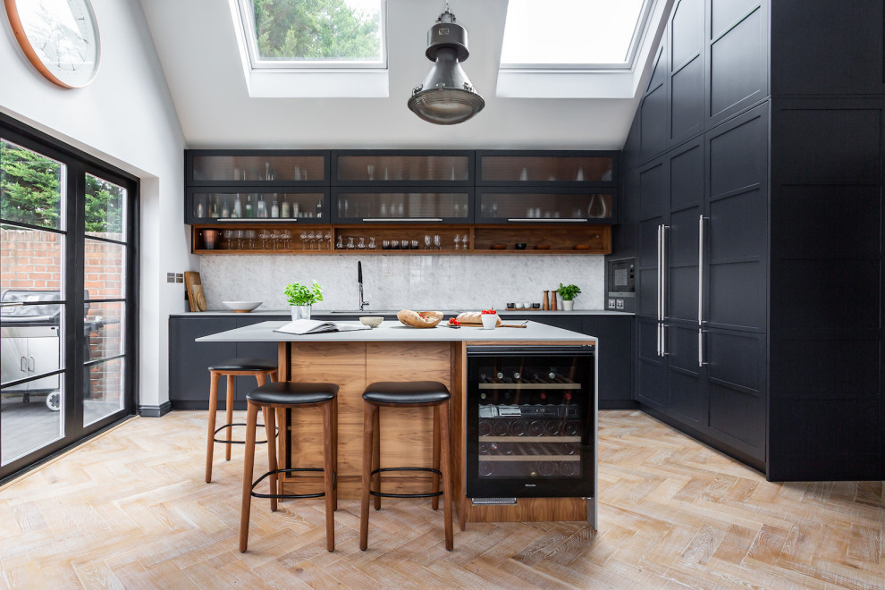 Inspiration för små klassiska grått kök med öppen planlösning, med luckor med upphöjd panel, grå skåp, bänkskiva i koppar, vitt stänkskydd, stänkskydd i marmor, svarta vitvaror, ljust trägolv och en köksö