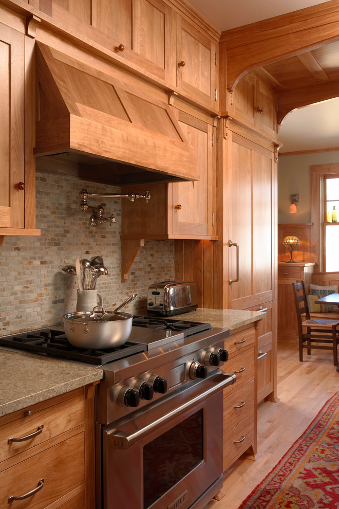 Amerikansk inredning av ett kök och matrum, med luckor med infälld panel, skåp i ljust trä, grått stänkskydd, rostfria vitvaror, mellanmörkt trägolv, granitbänkskiva, en rustik diskho och stänkskydd i skiffer