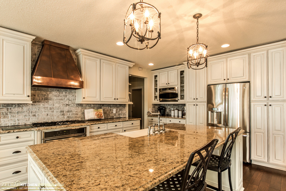 Eat-in kitchen - huge traditional l-shaped medium tone wood floor eat-in kitchen idea in Orlando with raised-panel cabinets, an undermount sink, white cabinets, granite countertops, gray backsplash, stone tile backsplash, stainless steel appliances and an island