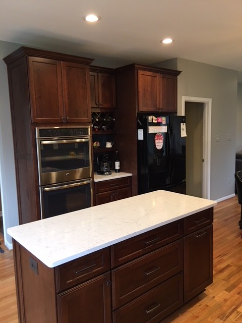 This is an example of a medium sized classic l-shaped kitchen/diner in Baltimore with a submerged sink, raised-panel cabinets, dark wood cabinets, engineered stone countertops, grey splashback, glass tiled splashback, stainless steel appliances, light hardwood flooring, an island and brown floors.