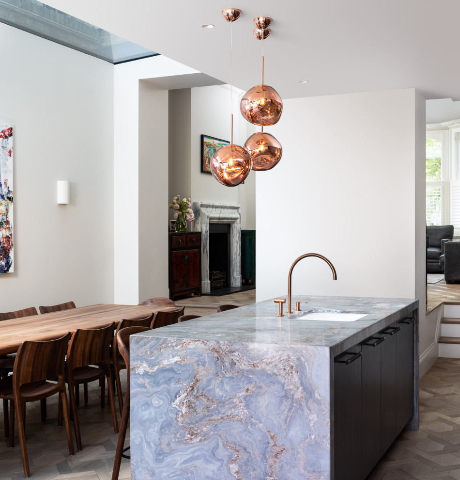 Contemporary single-wall kitchen/diner in London with a single-bowl sink, dark wood cabinets, grey splashback, marble splashback, medium hardwood flooring, an island, brown floors and grey worktops.