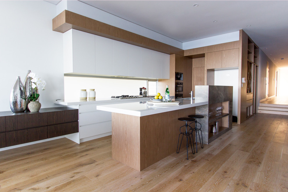 Exempel på ett mellanstort modernt kök, med en undermonterad diskho, släta luckor, vita skåp, rostfria vitvaror, ljust trägolv och en köksö