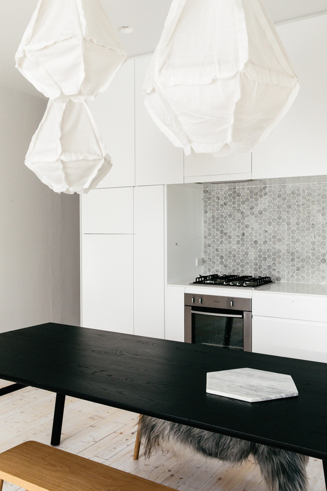 Inspiration for a scandi single-wall kitchen/diner in Sydney with grey splashback, stone tiled splashback, black appliances and light hardwood flooring.