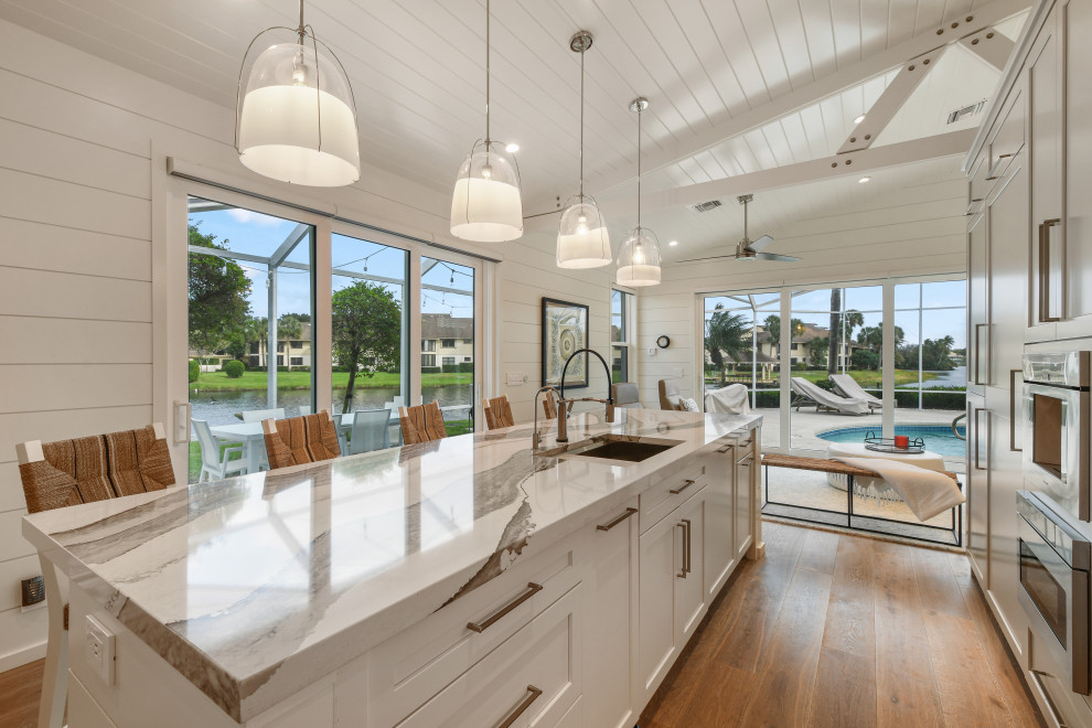 Design ideas for a medium sized beach style l-shaped open plan kitchen in Other with a submerged sink, grey cabinets, engineered stone countertops, stainless steel appliances, light hardwood flooring, an island, grey floors and white worktops.