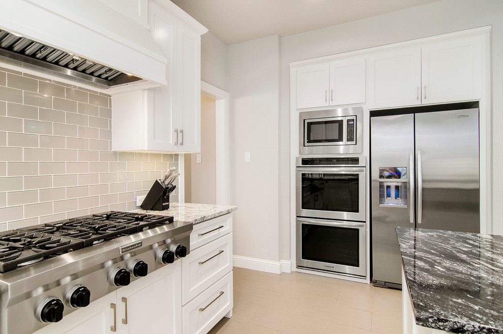 Example of a mid-sized minimalist u-shaped medium tone wood floor eat-in kitchen design in Dallas with an undermount sink, shaker cabinets, white cabinets, granite countertops, gray backsplash, ceramic backsplash, stainless steel appliances and an island