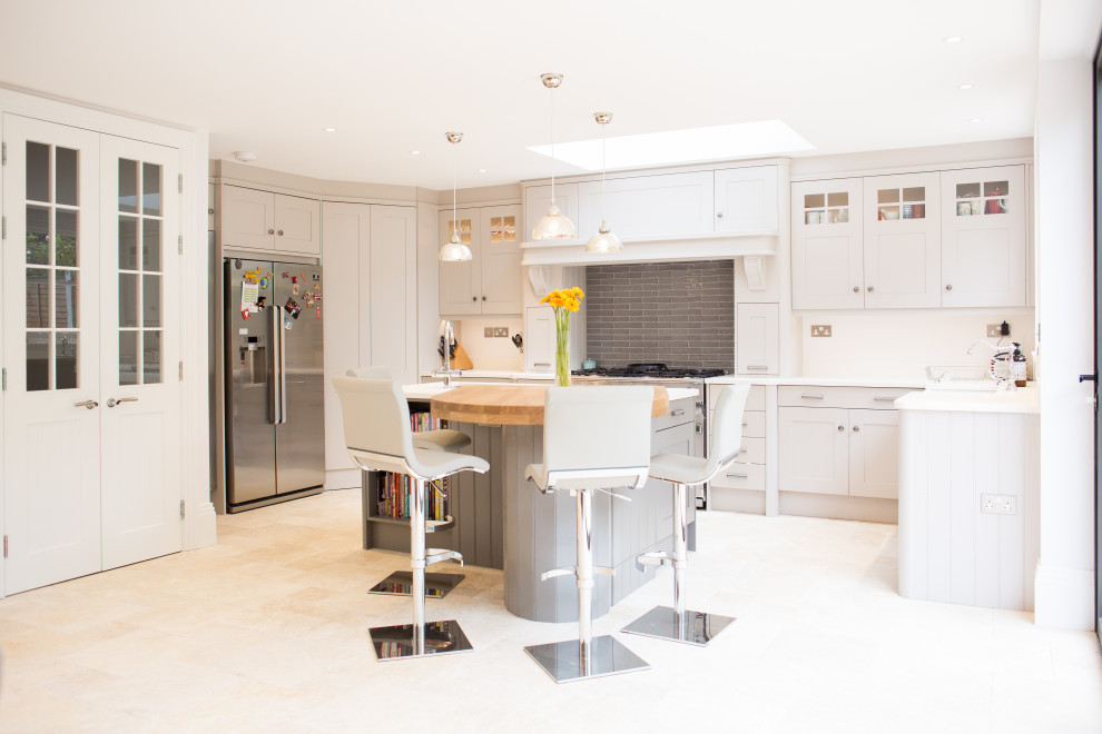 Medium sized traditional l-shaped open plan kitchen in London with a submerged sink, shaker cabinets, beige cabinets, composite countertops, grey splashback, metro tiled splashback, stainless steel appliances, ceramic flooring, an island, beige floors and white worktops.