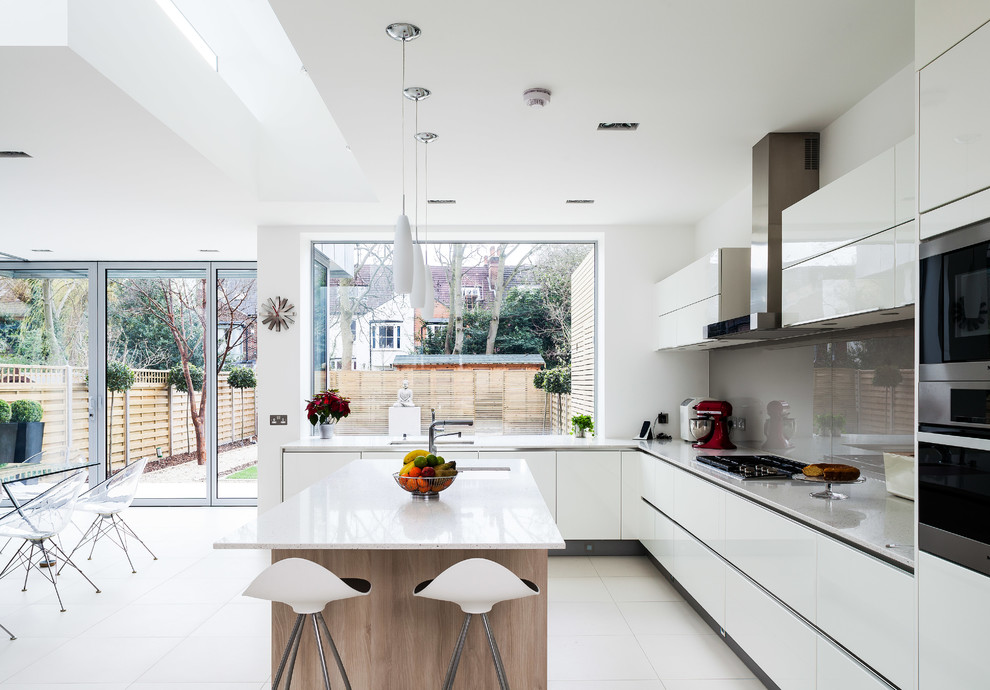 Moderne Küche mit Unterbauwaschbecken, flächenbündigen Schrankfronten, weißen Schränken, Küchenrückwand in Grau, Glasrückwand, Küchengeräten aus Edelstahl und Kücheninsel in London