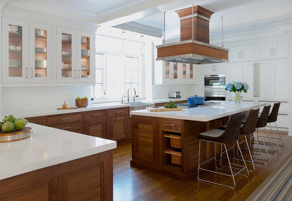 Klassische Küche in U-Form mit Landhausspüle, Glasfronten, weißen Schränken, Küchenrückwand in Weiß, Elektrogeräten mit Frontblende, braunem Holzboden und Kücheninsel in New York