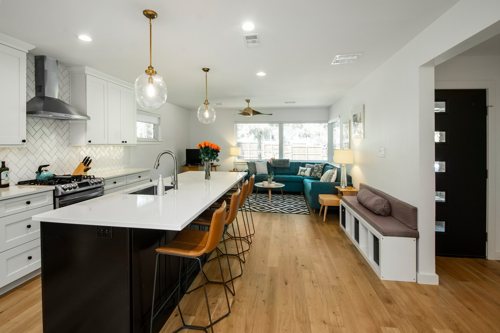 Medium sized single-wall open plan kitchen in Dallas with flat-panel cabinets, white cabinets, white splashback, stainless steel appliances, medium hardwood flooring, an island, brown floors, white worktops, a single-bowl sink, engineered stone countertops and ceramic splashback.