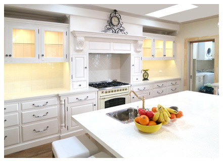 Klassisk inredning av ett stort linjärt kök med öppen planlösning, med en enkel diskho, luckor med glaspanel, vita skåp, vitt stänkskydd, stänkskydd i keramik, vita vitvaror, mellanmörkt trägolv och en köksö