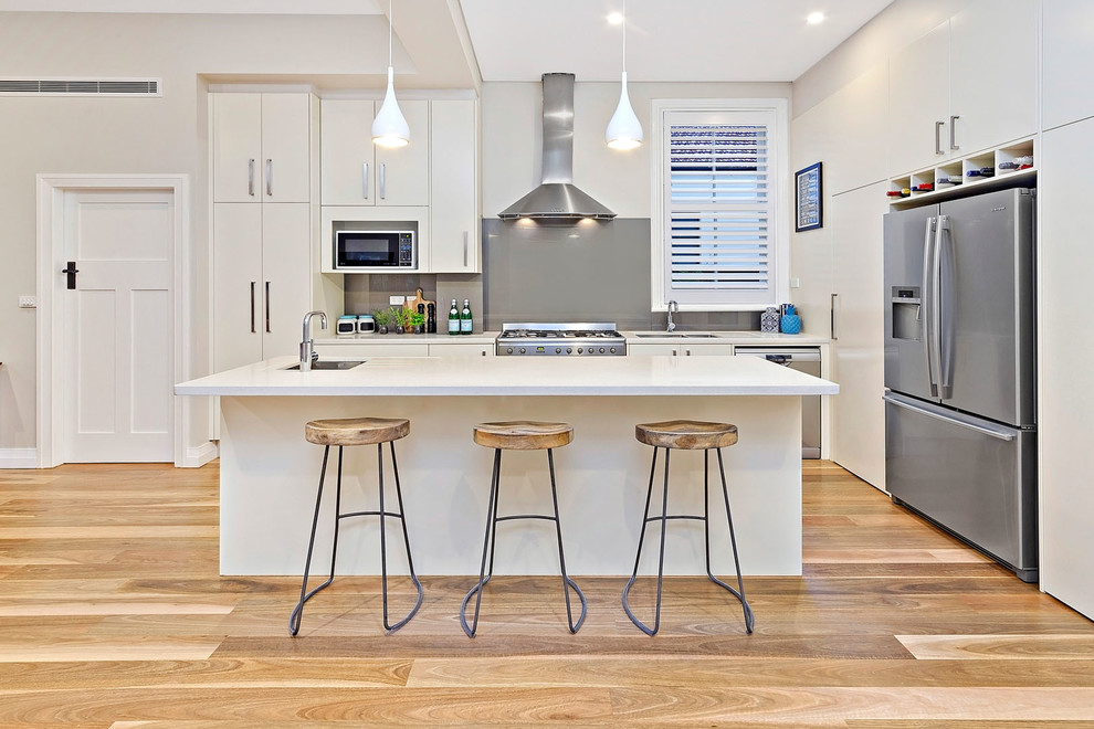 Design ideas for a contemporary l-shaped kitchen in Sydney with a submerged sink, flat-panel cabinets, white cabinets, grey splashback, stainless steel appliances, medium hardwood flooring and an island.
