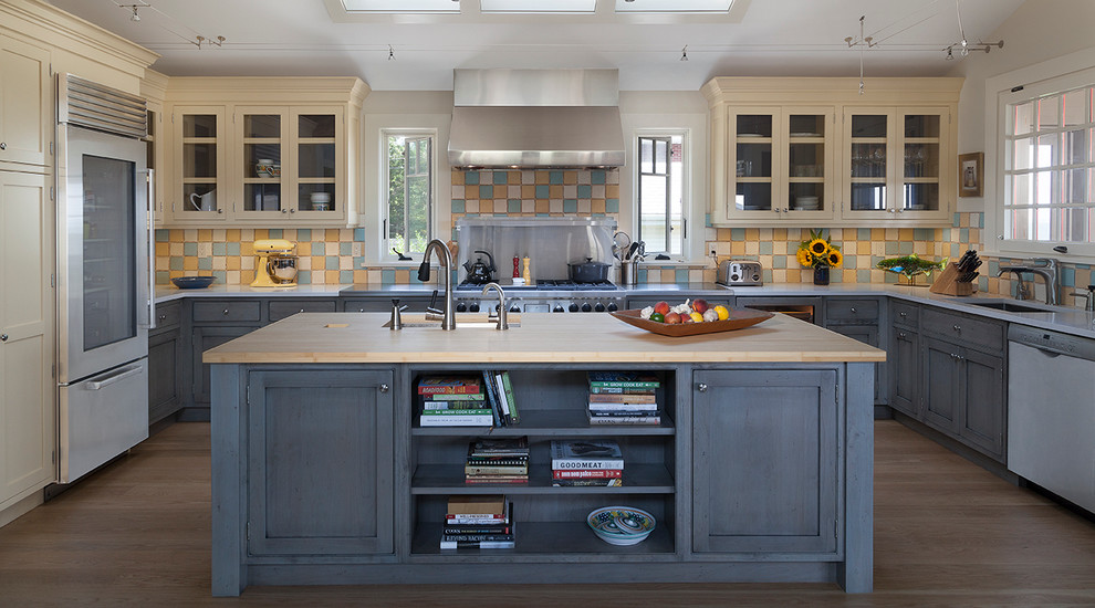 Mid-sized farmhouse u-shaped eat-in kitchen photo in New York with an undermount sink, beaded inset cabinets, yellow cabinets, wood countertops, multicolored backsplash, stainless steel appliances and an island