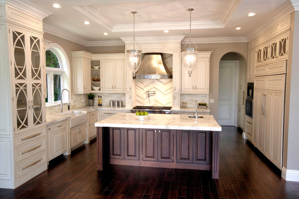 Example of a large classic u-shaped dark wood floor and brown floor enclosed kitchen design in San Francisco with a farmhouse sink, raised-panel cabinets, white cabinets, quartzite countertops, multicolored backsplash, matchstick tile backsplash, paneled appliances and an island