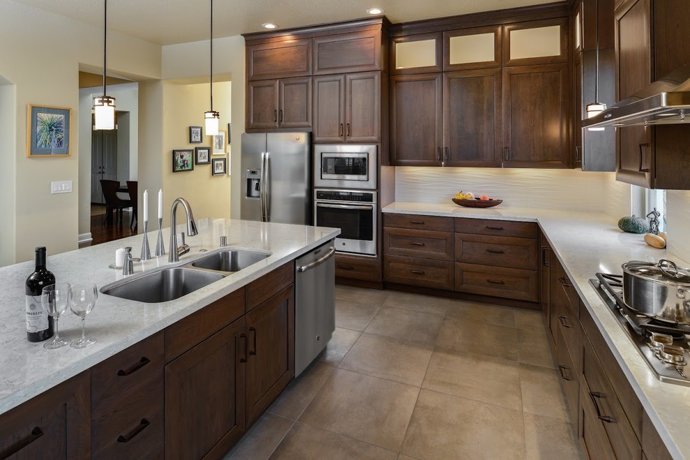 Large traditional l-shaped kitchen/diner in Sacramento with a double-bowl sink, recessed-panel cabinets, dark wood cabinets, marble worktops, white splashback, stainless steel appliances, concrete flooring, an island and grey floors.