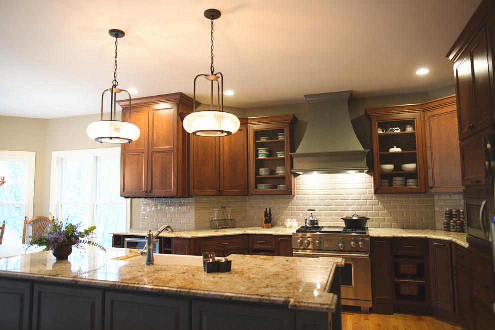 Example of a large classic single-wall medium tone wood floor eat-in kitchen design in Boston with a farmhouse sink, recessed-panel cabinets, dark wood cabinets, granite countertops, white backsplash, subway tile backsplash, stainless steel appliances and an island